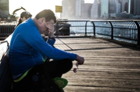 A sad man sitting on a bench on a river side in a city