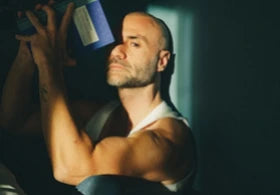 A depressed man sitting on the ground, being lit up by a single sun beam.